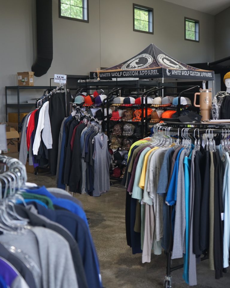 Custom apparel showroom by White Wolf Custom Apparel in Minnesota – clothing racks, hats, and branded merchandise display